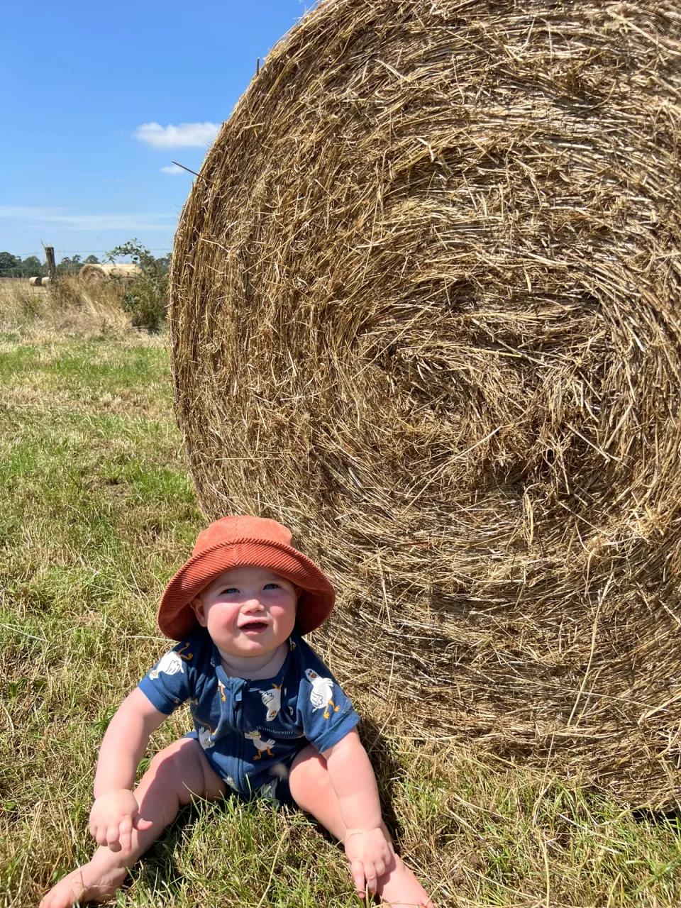 George, all smiles in a sun hat, sitting beside a big round bale